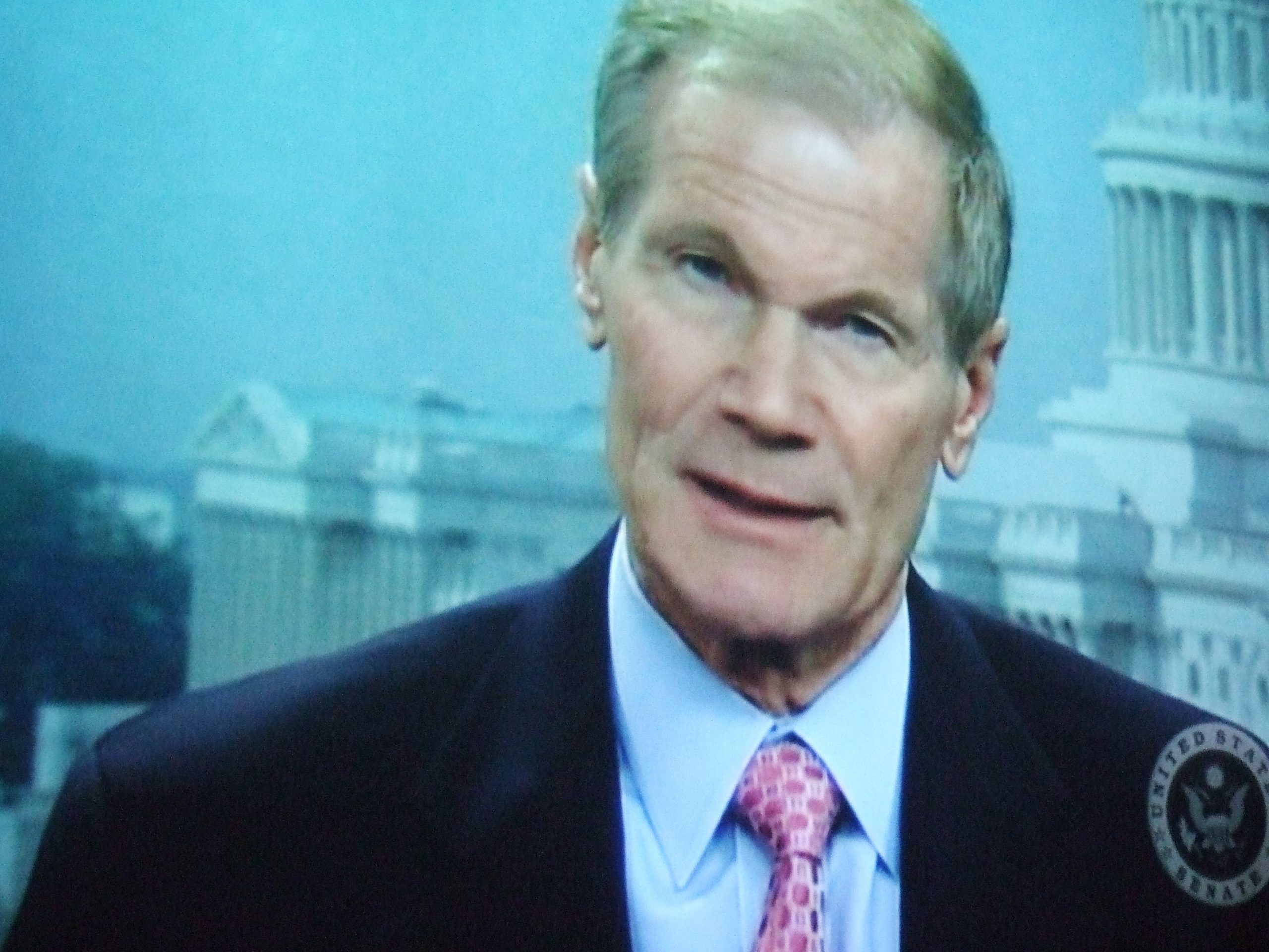 Screenshot of Nelson mid-word in front of a background of the United States Capitol Building. The Senate Seal is stamped on the lower-right corner.