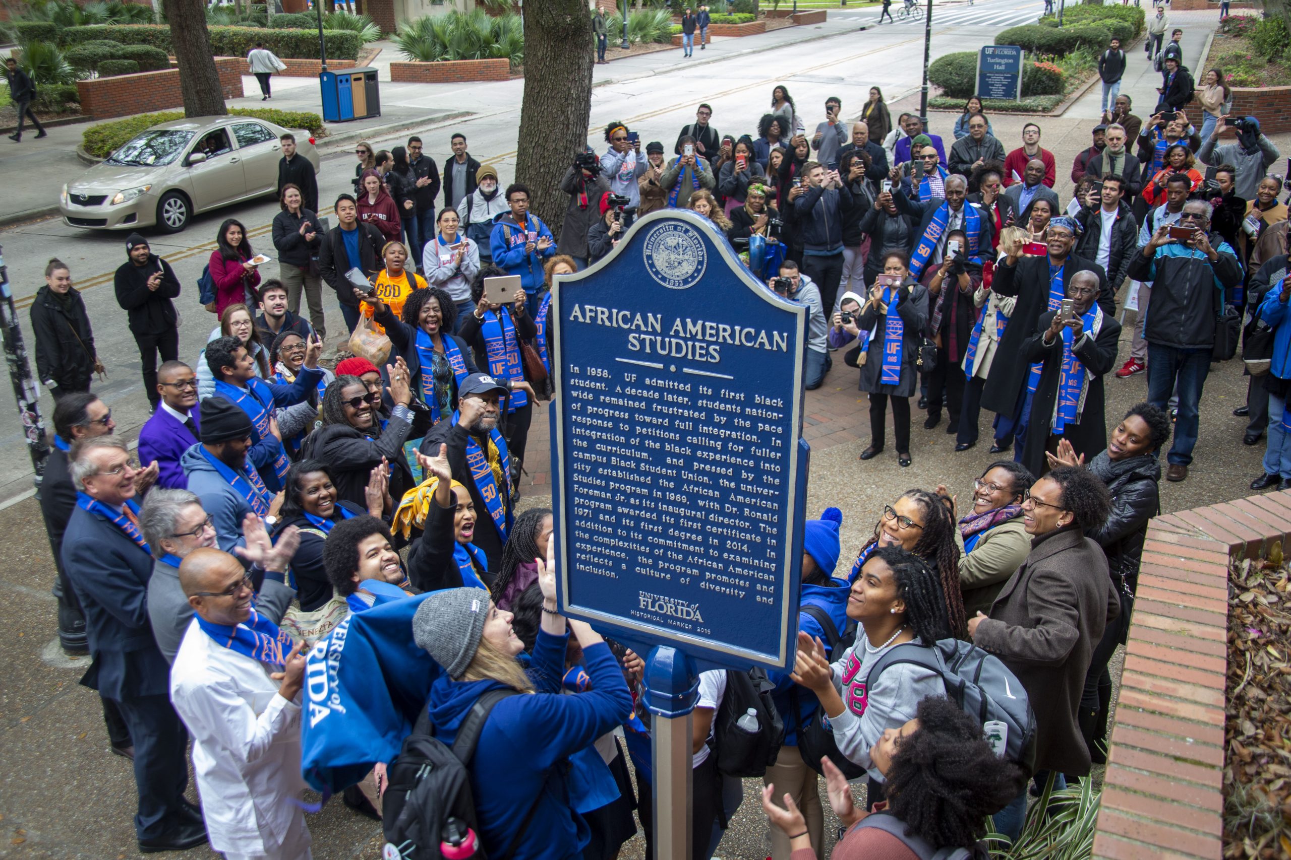 A large group surrounds a blue sign that reads “African American Studies,” followed by additional text. Much of the group is smiling and clapping.