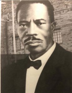 Sepia photo of Reverend Mason. He wears a black jacket, white shirt, and black bowtie. He is looking beyond the camera, not smiling.
