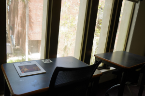 A char and desk facing a floor to ceiling window overlooking campus
