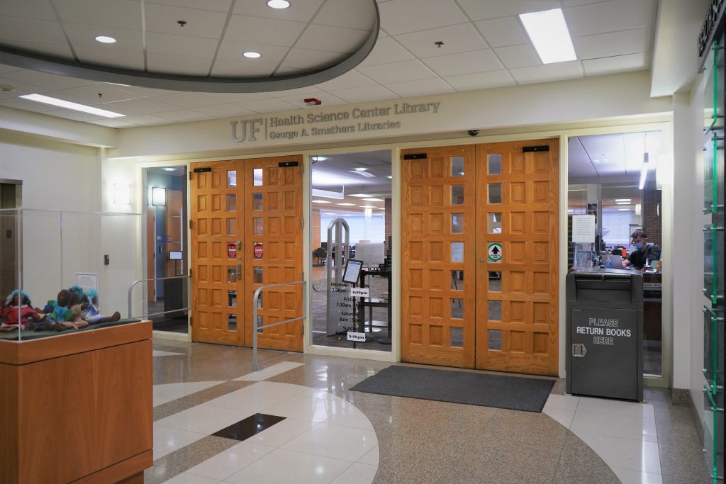 Two sets of wooden doors that pop out compared to their white and grey surroundings. Above the doors, a sign reads "Health Science Center Library, George A. Smathers Libraries"