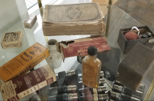 Several historic medial items in a glass case, including glass bottles of "Dr Porter's Antiseptic Healing Oil" and "Hamlin's Wizard Oil Linment," bandages, and an old thick book called The People's Medical Adviser