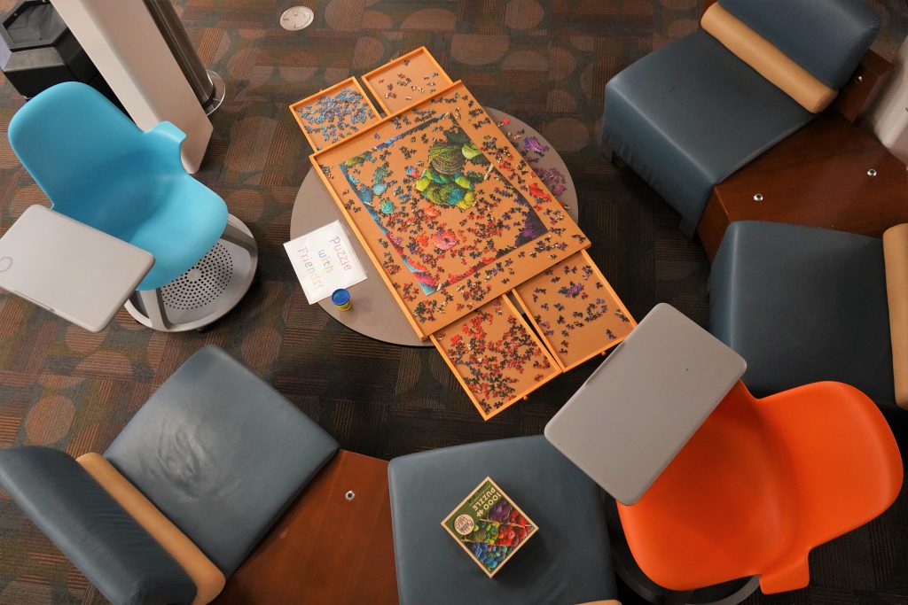 Overhead look of a small round table surrounded by colorful chairs. On the table is a half assembled jigsaw puzzle.