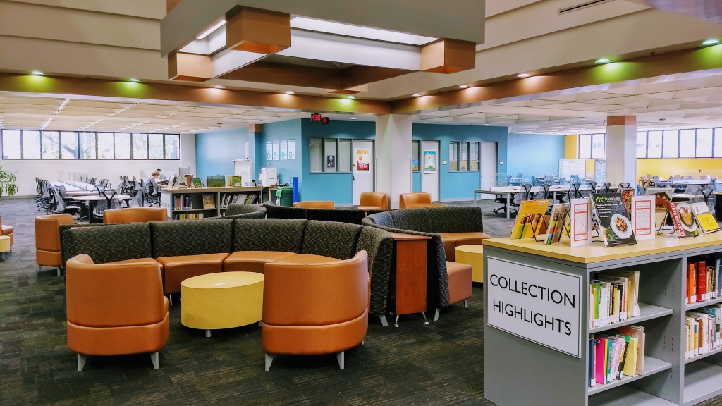 A colorful library space featuring round tables, chairs, and a "collection highlights" bookself