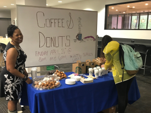 A table covered in trays of donut holes and Starbucks coffee. A library worker smiles while a student pours a cup.