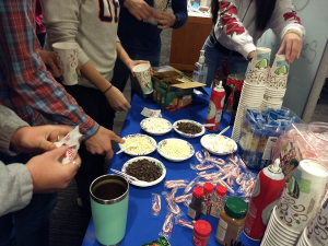 Bowls of chocolate chips, marshmellows, candy canes, sprinkles, and whipped cream next to coffee cups and hot chocolate packages
