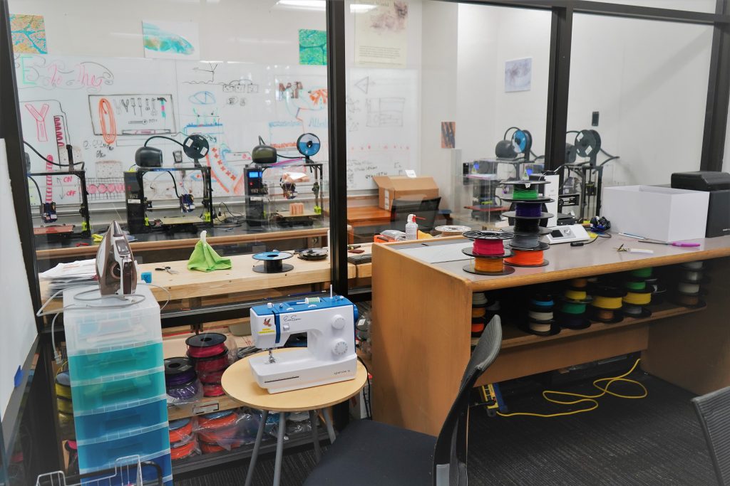 A busy room full of crafting material, including a sewing machine, 3D printers, and spools of plastic filament