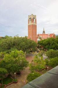 A brick belltower stands high over walkways, trees, and other building