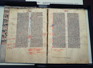 An open face book with text in Latin. There are lots of annotations in red ink. The pages are aged, with brown edges.