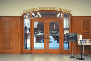 Wooden paneled walls and wooden doors. Above the doors reads "Grand Reading Room." On the door is a doorbell with a sign that says "Department of Special Collections Reading Room"