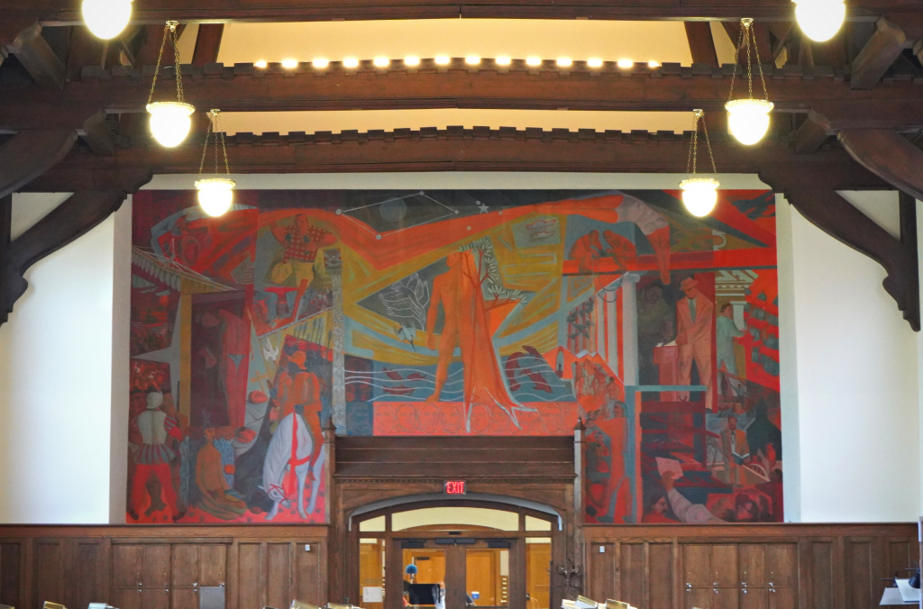 A large mural above the main entrance door with numerous small scenes surrounding a person in bright orange