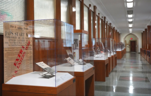 A long hallway with a row of glass museum cases against the wall holding books, pictures, and newspapers