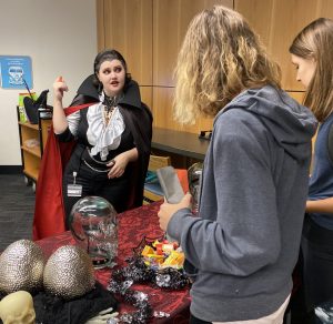 A library worker in a Count Dracula costume with slicked back hair and red lipstick gives away candy to visiting students