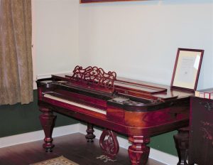 A square grand piano, made out of reddish wood, at the Scott Joplin House State Historic Site.