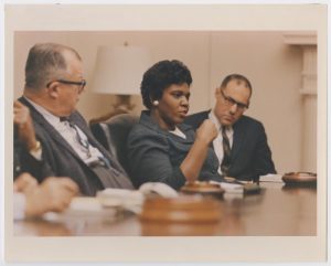 Barbara Jordan seated at a table between two men. They are at a meeting in Washington, D.C. to preview President Lyndon B. Johnson's plan on civil rights for 1967.