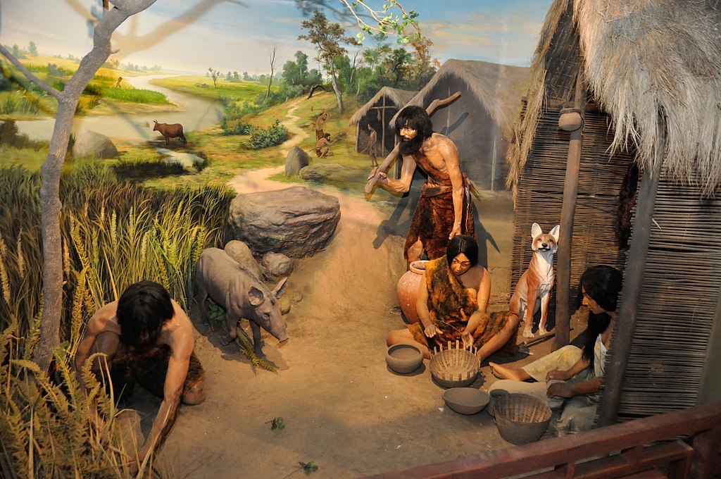 diorama of a neolithic village with people, pots and baskets, dog