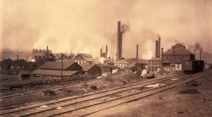 Smokestacks and buildings by rail lines in sepia