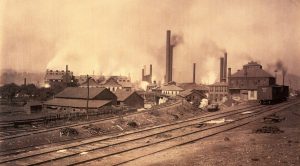 Smokestacks and buildings by rail lines in sepia 