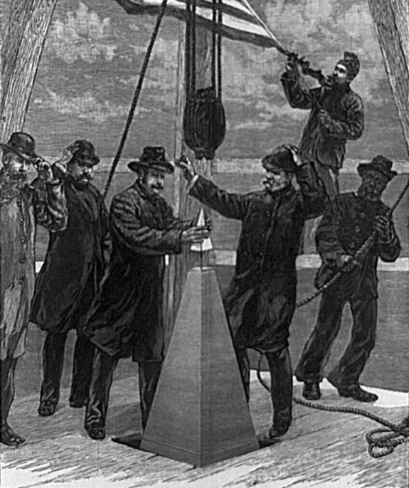 Grayscale illustration of group of men, some using ropes and pulleys, others tipping their hats as one man places top of monument. 