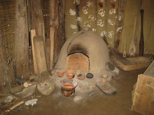 Reconstructed Neolithic house interior, clay or earth wall, hearth/oven and pottery