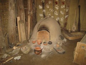 Reconstructed Neolithic house interior, clay or earth wall, hearth/oven and pottery 