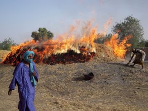 Malian man walking in foreground with flames over open pit clay firing