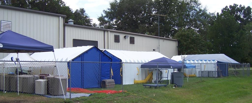 Three carport-size disaster response tents set up behind a shelter building.