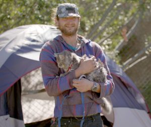 Justin and his cat Um standing outside their tent home in the streets of Los Angeles