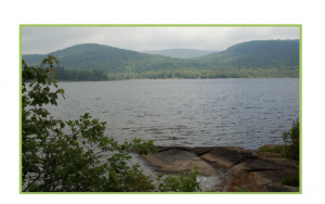 Color photograph of a lake in front of green rolling mountains.