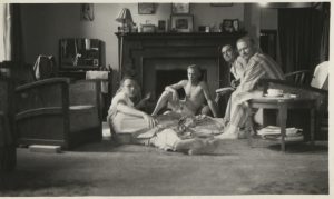 Black and white photograph of four men; two are sitting on the floor, and two are sitting on chairs.