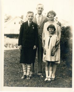Sepia photograph of the MacDonald family, who are wearing formal clothing and standing in front of their home.