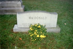 Color photograph of a bottle and yellow roses in front of MacDonald's grave.
