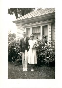 Black and white photograph of John, in a black jacket and white pants, with his arm around Dorothy, in a white dress and holding flowers.