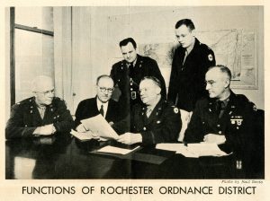 Newspaper clipping showing a black and white photograph of six men in military uniform looking at documents. Text reads: Function of Rochester Ordinance District.